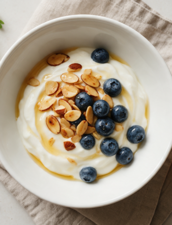 Overhead view of a skyr bowl topped with toasted almonds, fresh blueberries and a honey drizzle on a linen napkin