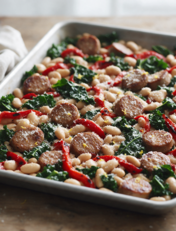 Overhead shot of roasted chicken sausage coins, cannellini beans, red peppers and kale on a rimmed sheet pan