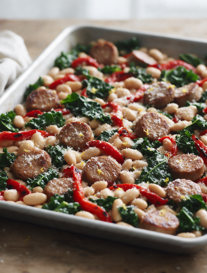 Overhead shot of roasted chicken sausage coins, cannellini beans, red peppers and kale on a rimmed sheet pan