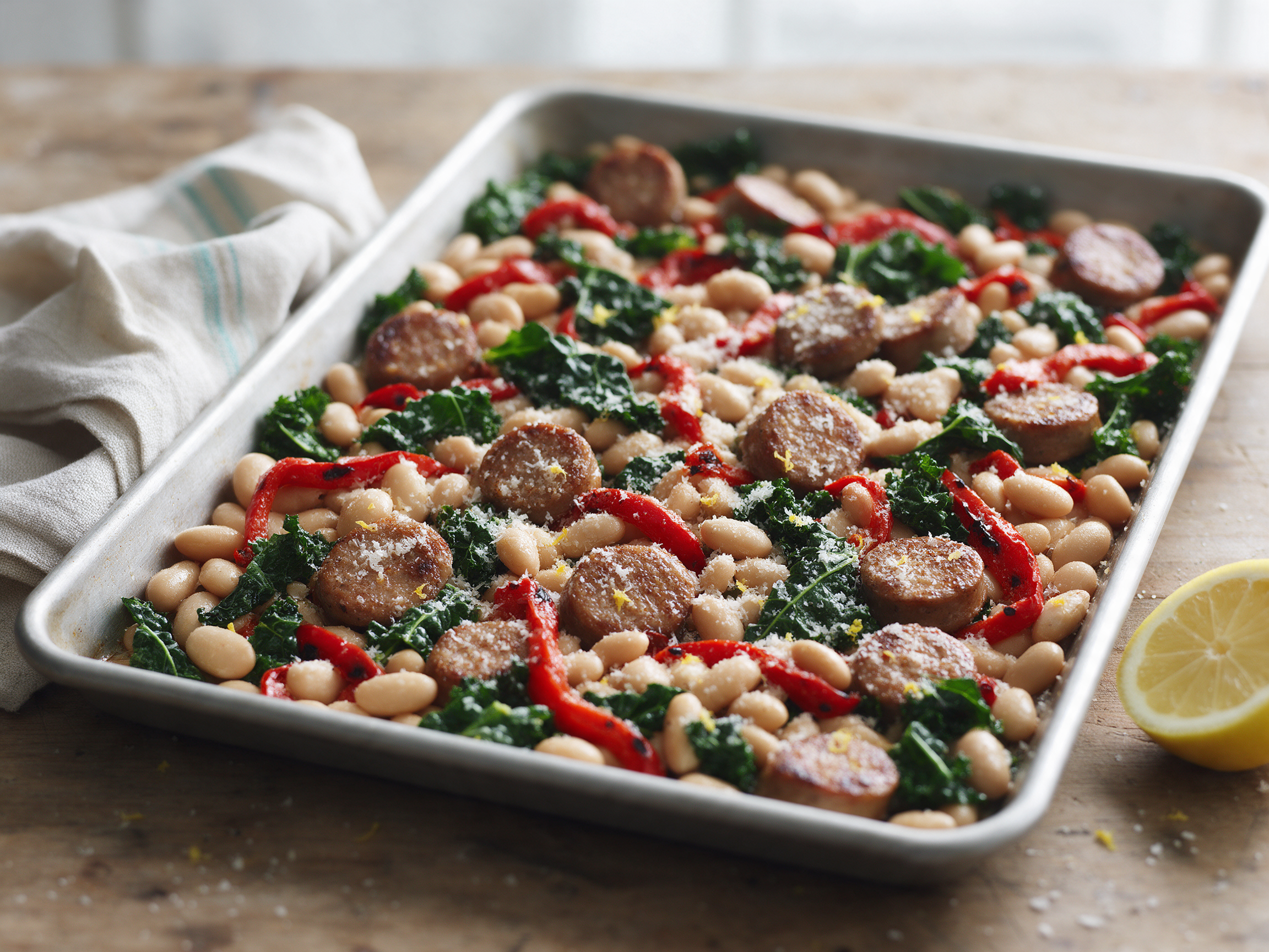 Overhead shot of roasted chicken sausage coins, cannellini beans, red peppers and kale on a rimmed sheet pan